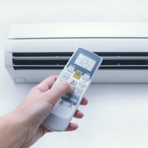 A hand holding a remote control for a mini-split air conditioner that is on the wall.