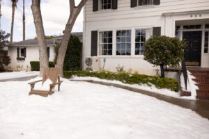 white residential house with a mini-split air conditioner on the ground at the left corner. Snow covers the front yard.