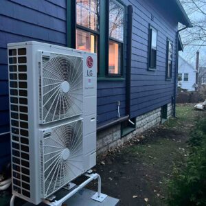 A mini-split air conditioning unit installed outside a dark blue residential home.