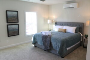 Bedroom with a queen bed and a window with a mini-split air conditioner on the wall.