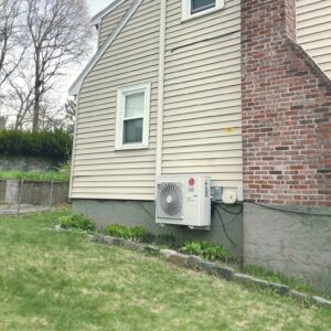 Mini-split air conditioner mounted on the side of a residential home near the ground.