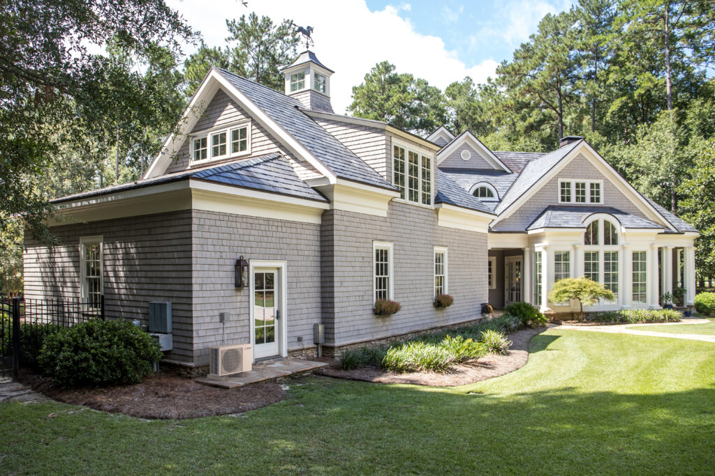 The front exterior view of a large, ranch style, residential home with a ductless mini-split air conditioning unit installed at the far left.