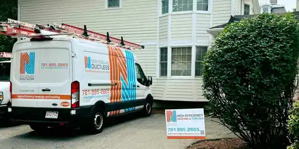 A white service van with orange and blue branding, including a logo and text, has ladders on its roof rack and is parked in front of a light-colored building.